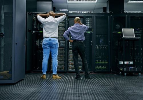 man standing with hands on head next to a nother man staring at servers in a server room